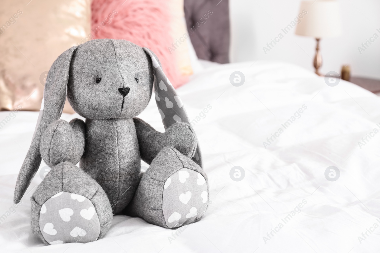 Photo of Cute toy rabbit on bed in child's room interior. Space for text