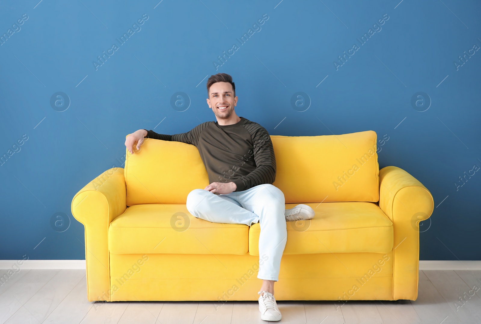 Photo of Handsome young man sitting on sofa, indoors