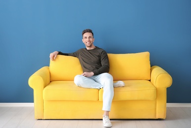 Photo of Handsome young man sitting on sofa, indoors