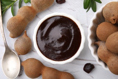 Photo of Bowl of tasty tamarind sauce and fresh pods on white textured table, flat lay