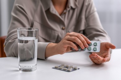 Woman holding blister of antidepressant pills near glass of water at white table, closeup