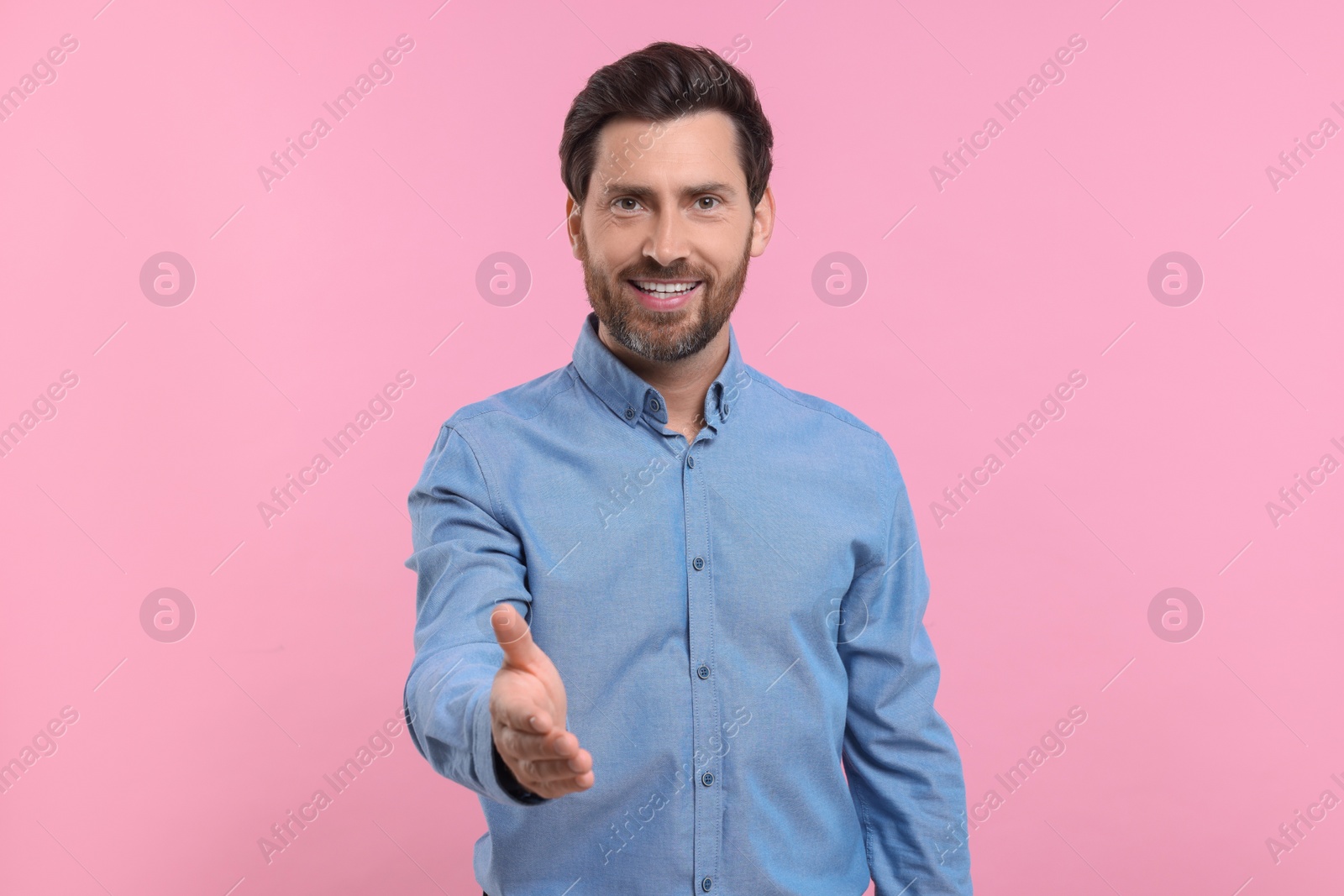 Photo of Happy man welcoming and offering handshake on pink background