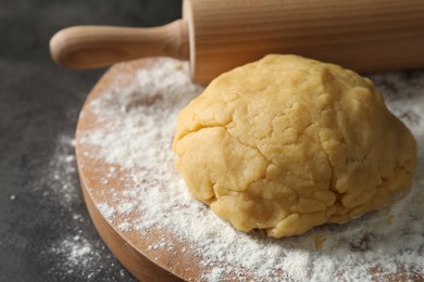 Making shortcrust pastry. Raw dough, flour and rolling pin on grey table, closeup