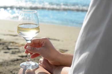 Photo of Woman with glass of tasty wine near sea, closeup
