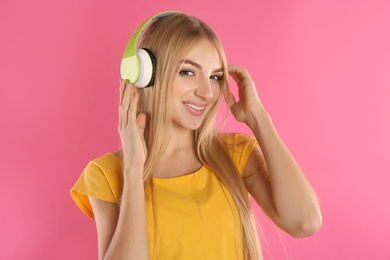 Beautiful young woman listening to music with headphones on color background