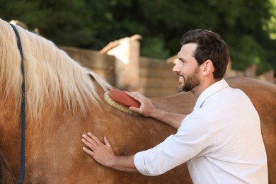 Man brushing adorable horse outdoors. Pet care