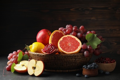 Photo of Wicker basket with different fruits and berries on black table