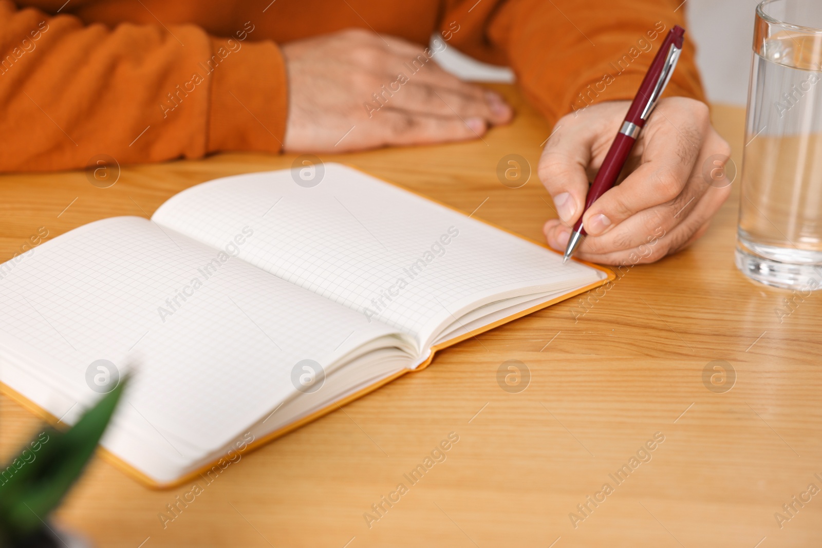 Photo of Young man writing in notebook at wooden table, closeup