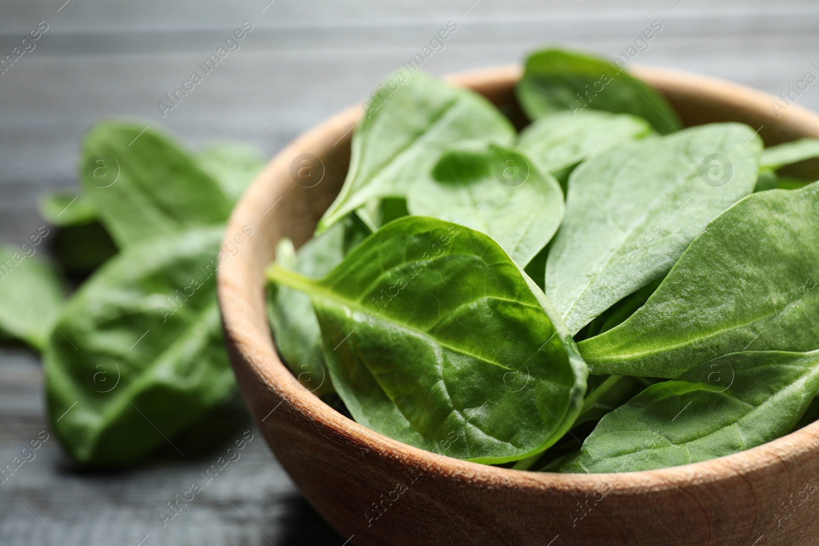 Photo of Bowl of fresh green healthy spinach on dark wooden table, closeup