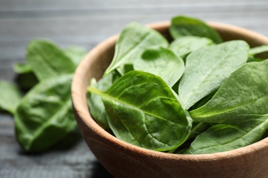 Bowl of fresh green healthy spinach on dark wooden table, closeup