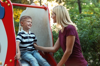 Photo of Nanny and cute little boy on slide outdoors