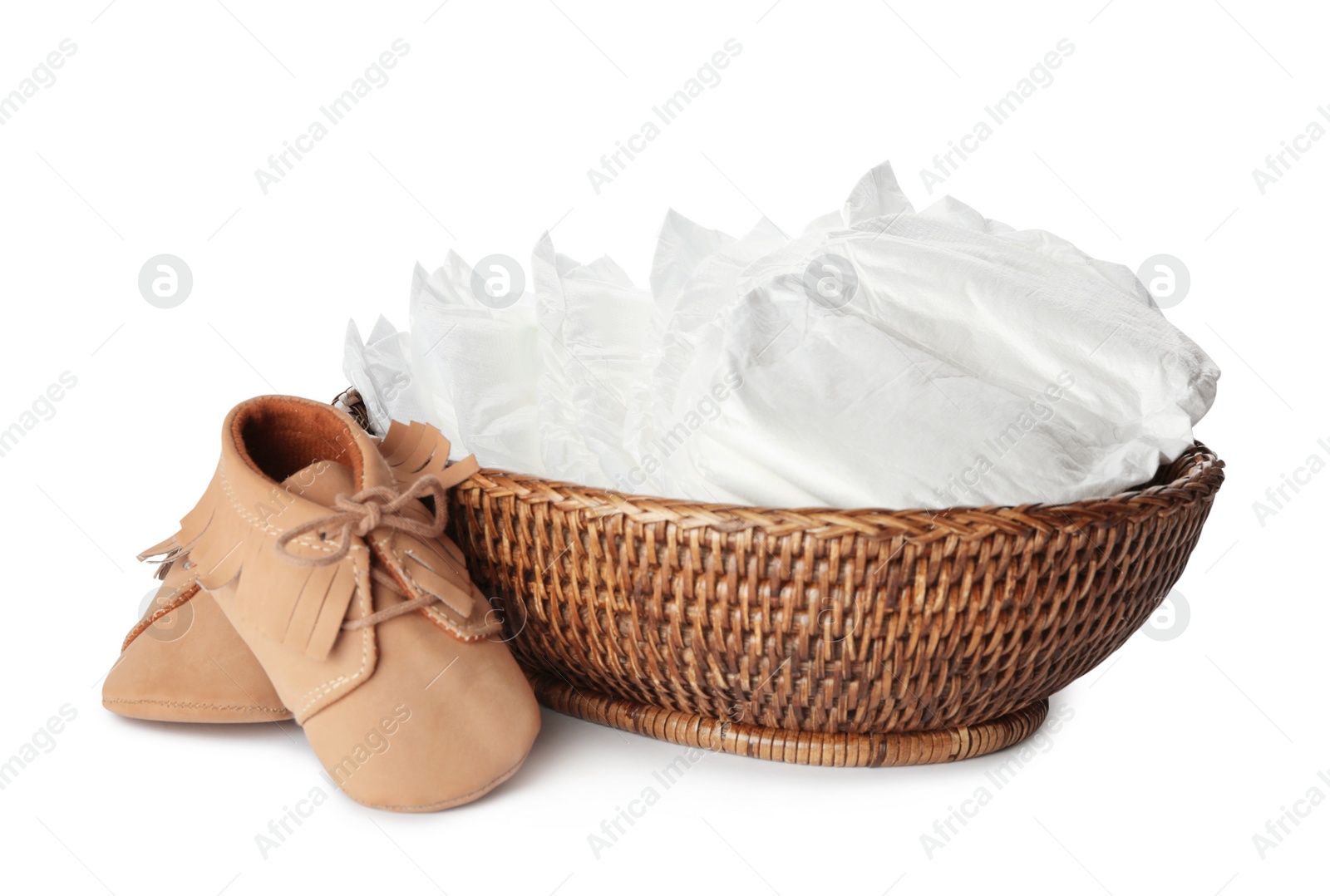Photo of Wicker bowl with disposable diapers and child's shoes on white background