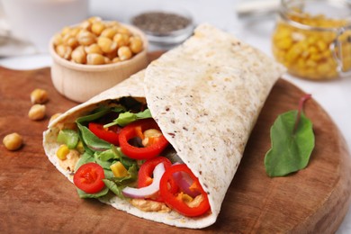 Delicious hummus wrap with vegetables on wooden board, closeup