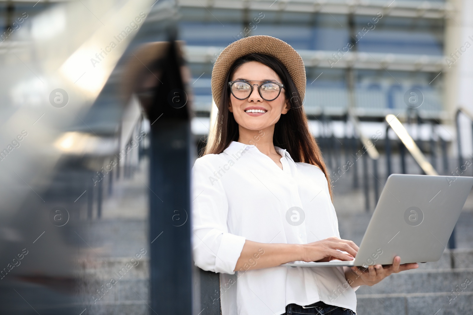 Photo of Beautiful woman with glasses using laptop on city street