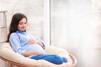 Photo of Beautiful pregnant woman sitting in lounge chair near window