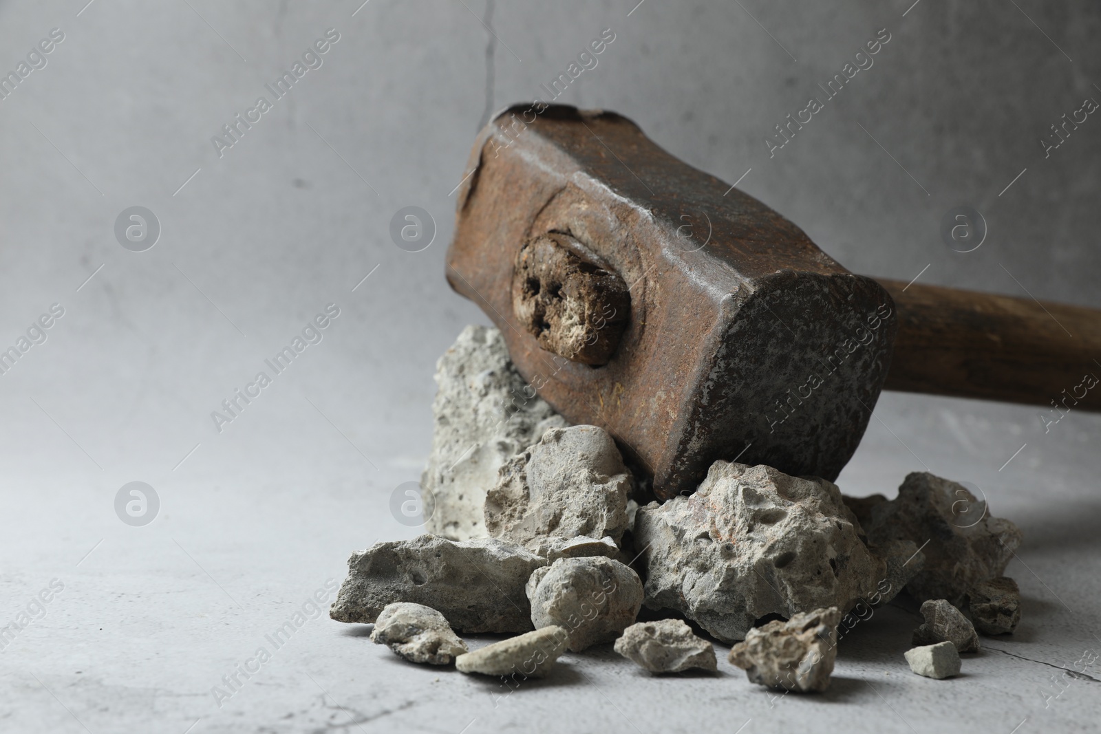 Photo of One sledgehammer and pieces of broken stones on grey background, closeup. Space for text