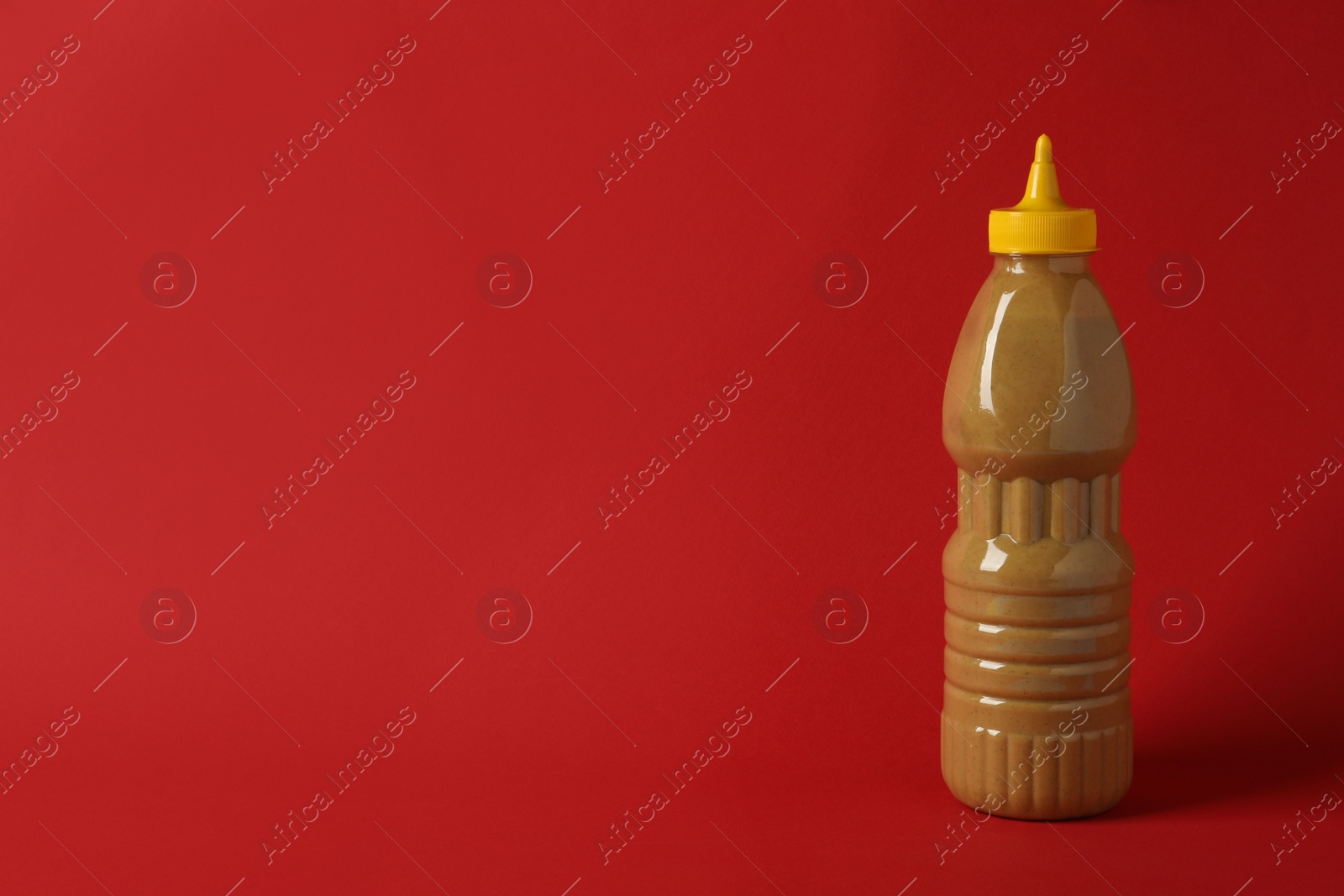 Photo of Spicy mustard in plastic bottle on red background, space for text
