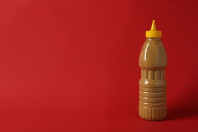 Spicy mustard in plastic bottle on red background, space for text