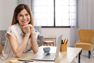 Photo of Young woman working with laptop at desk in home office