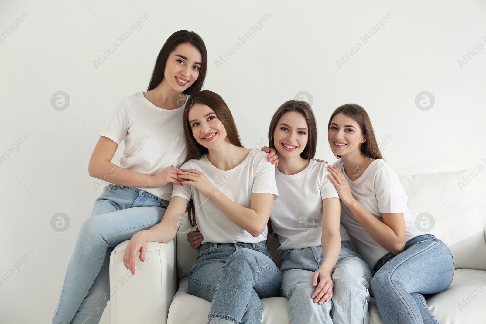 Photo of Beautiful young ladies in jeans and white t-shirts on sofa indoors. Woman's Day