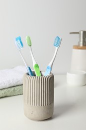 Photo of Plastic toothbrushes in holder, towels and cosmetic products on white countertop