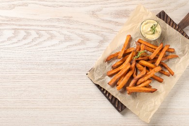 Photo of Board with delicious sweet potato fries and sauce on white wooden table, top view. Space for text