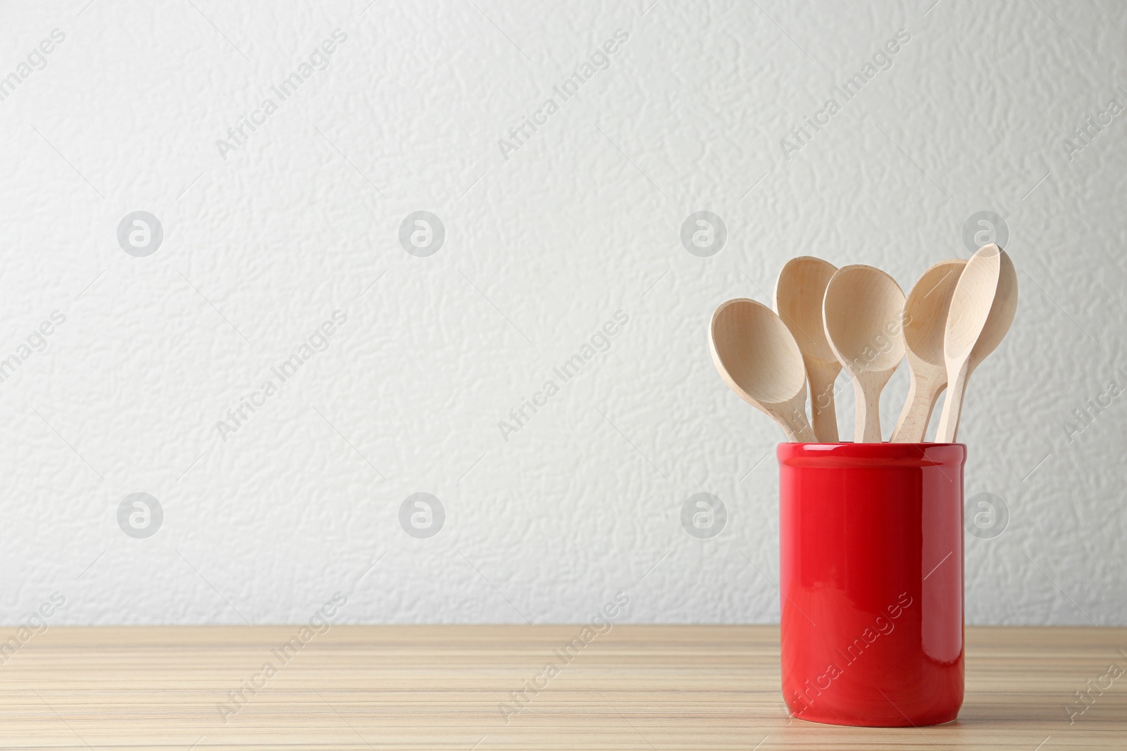 Photo of Set of kitchen utensils in stand on wooden table near light wall. Space for text