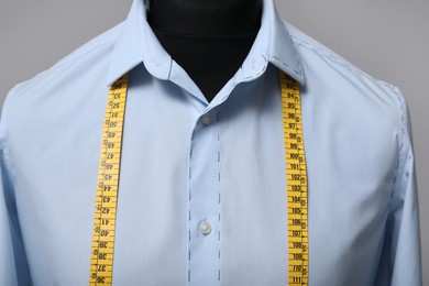 Photo of Semi-ready shirt with tailor's measuring tape on mannequin against grey background, closeup