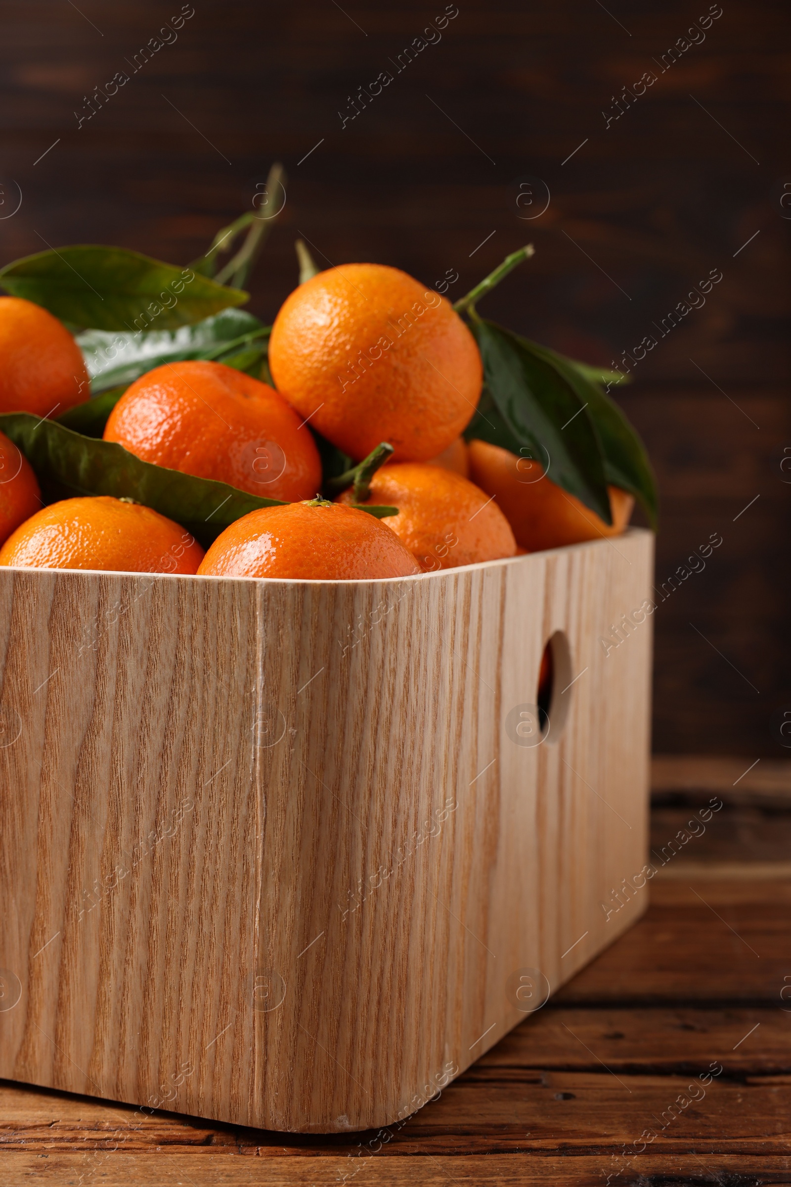 Photo of Fresh tangerines with green leaves in crate on wooden table, closeup