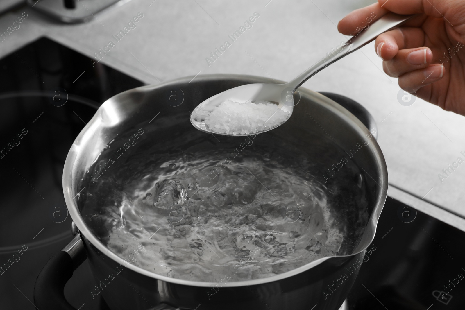 Photo of Woman salting boiling water in pot on stove, closeup