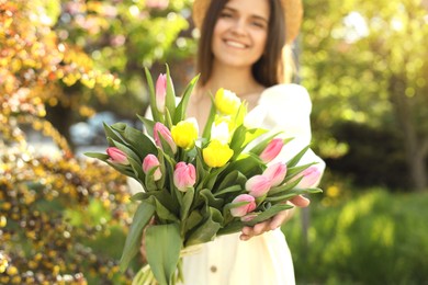 Photo of Beautiful young woman with bouquet of tulips in park, focus on flowers