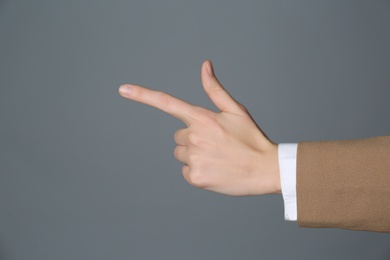 Businesswoman pointing at something on grey background, closeup. Finger gesture