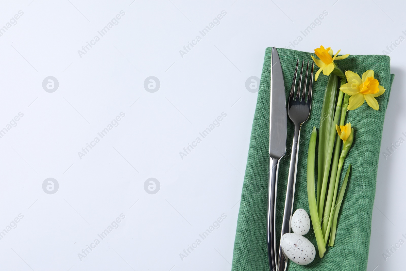 Photo of Cutlery set, Easter eggs and narcissuses on white background, top view with space for text. Festive table setting