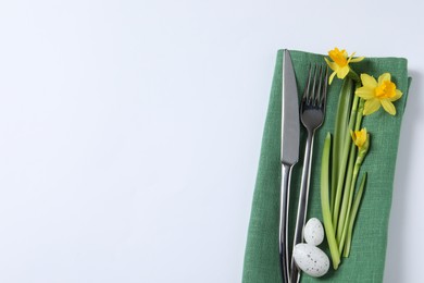 Cutlery set, Easter eggs and narcissuses on white background, top view with space for text. Festive table setting