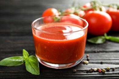 Glass of tomato sauce with basil on wooden table, closeup