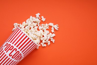 Bucket of tasty popcorn on orange background, flat lay. Space for text