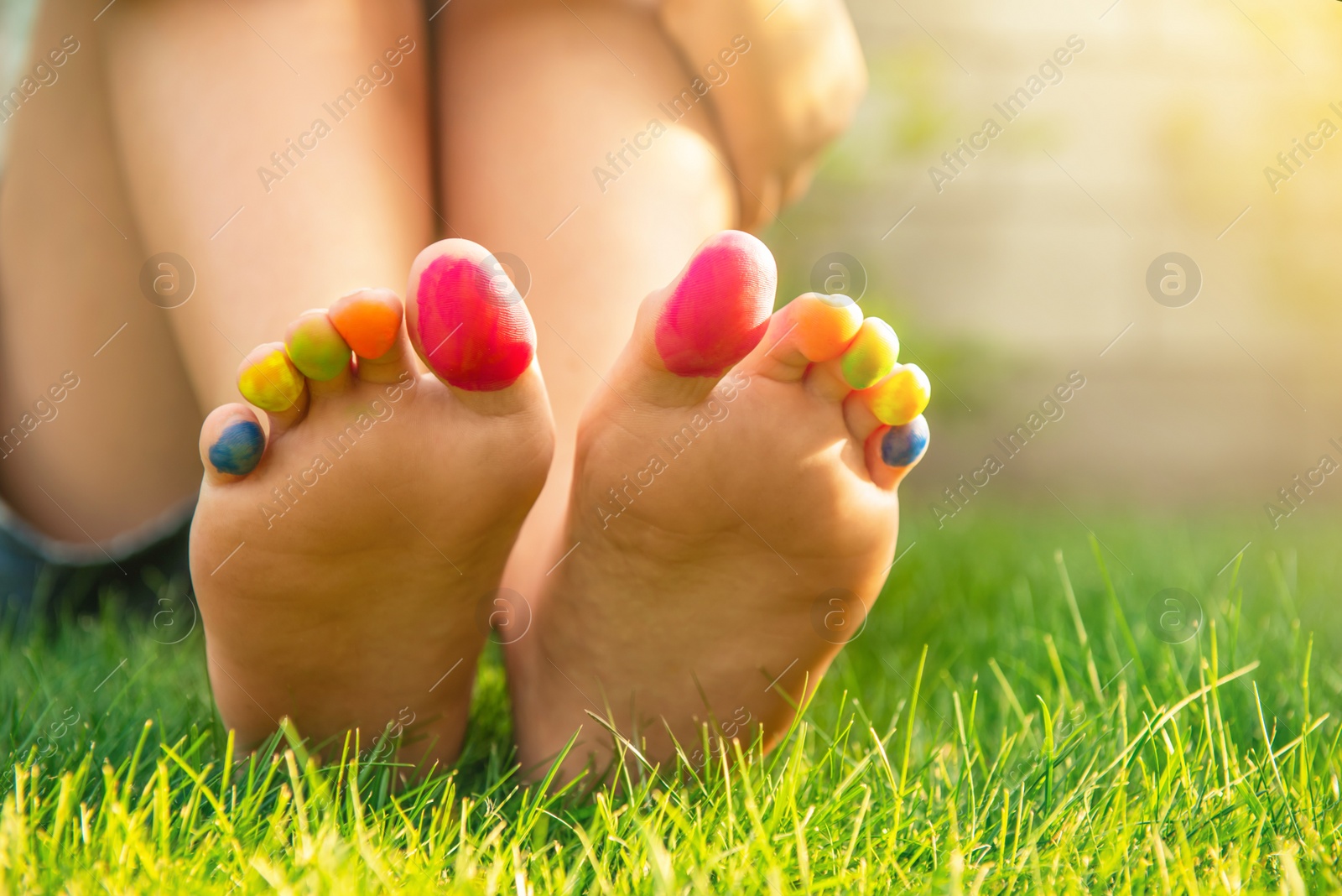 Photo of Teenage girl with painted toes sitting on green grass outdoors, closeup