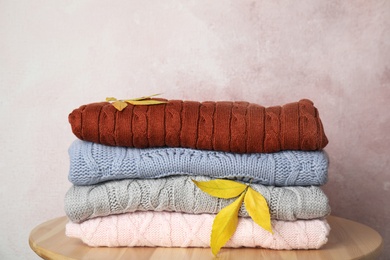 Photo of Stack of warm knitted clothes and autumn leaves on wooden table against light pink background