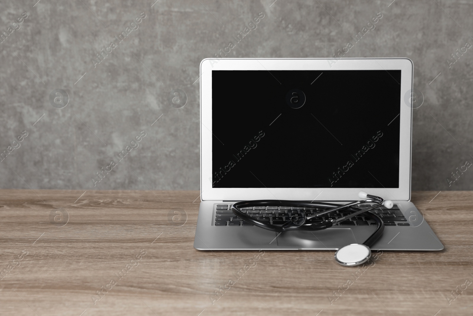 Photo of Laptop with blank screen and stethoscope on table against grey background, space for text. Computer repair