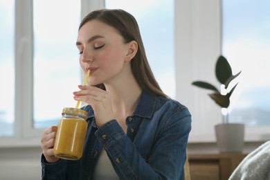 Photo of Beautiful young woman drinking delicious smoothie at home. Space for text