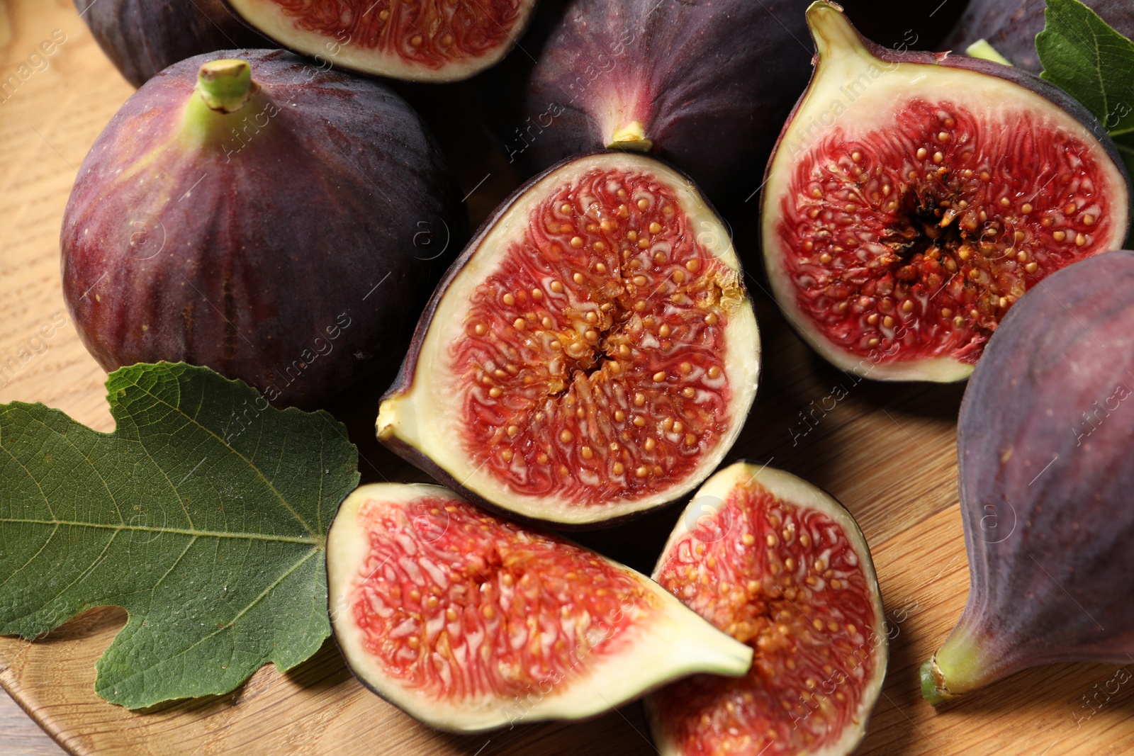 Photo of Whole and cut ripe figs with leaves on wooden table, closeup