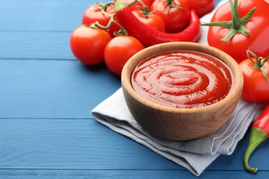 Photo of Bowl of tasty ketchup, tomatoes and peppers on blue wooden table, closeup. Space for text