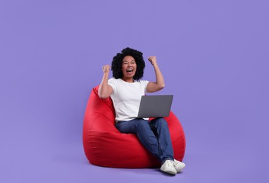 Photo of Emotional young woman with laptop sitting on beanbag chair against purple background