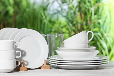 Photo of Set of clean dishware on white table against blurred background
