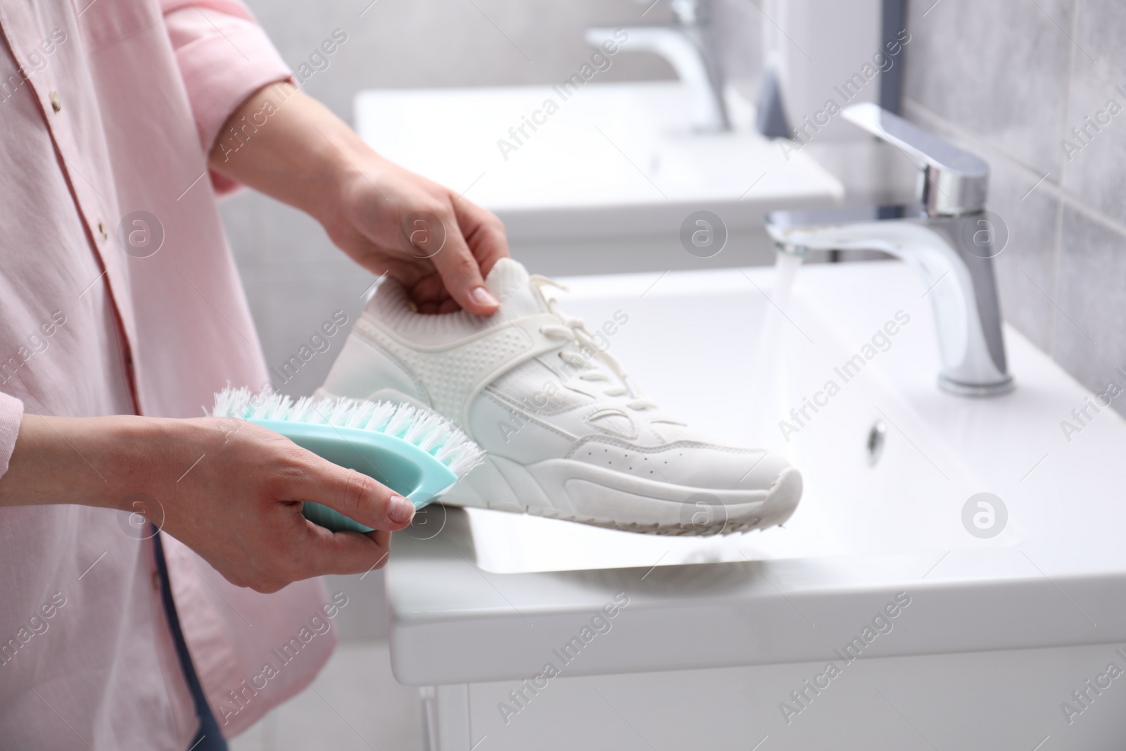 Photo of Woman washing stylish sneakers with brush in sink, closeup