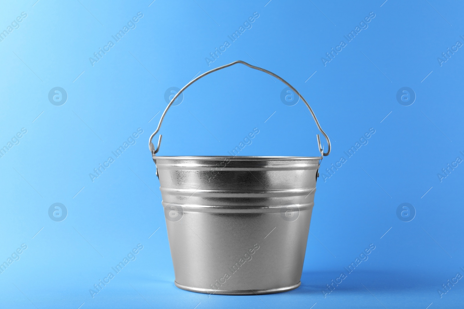 Photo of One shiny metal bucket on light blue background