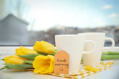 Photo of Aromatic coffee, beautiful flowers and GOOD MORNING wish on light windowsill