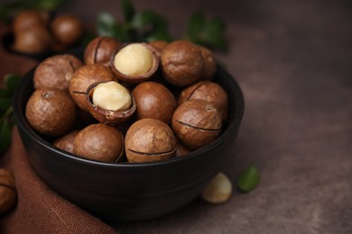 Photo of Tasty Macadamia nuts in bowl on brown table, closeup. Space for text