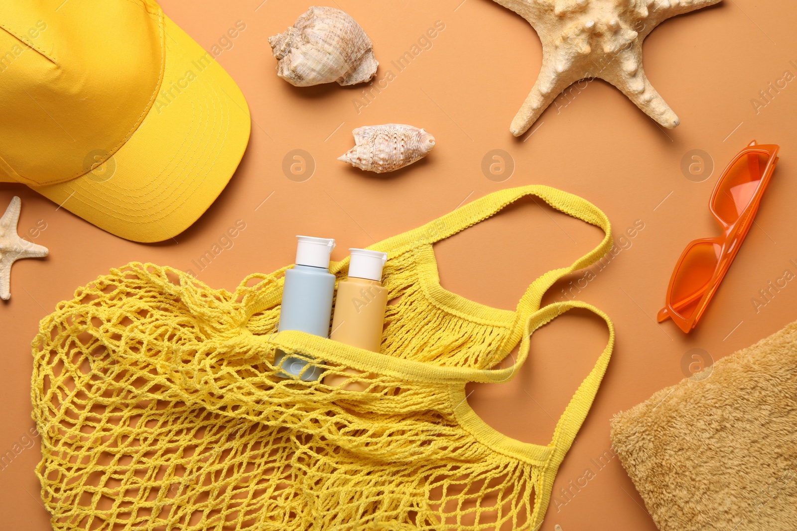 Photo of String bag and different beach accessories on pale orange background, flat lay