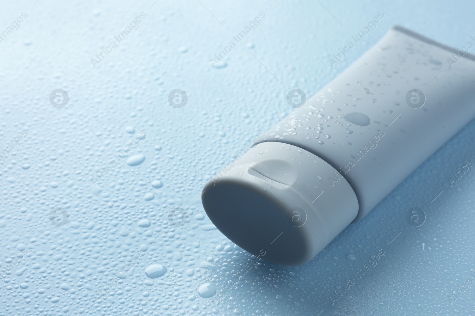 Photo of Moisturizing cream in tube on light blue background with water drops, closeup. Space for text